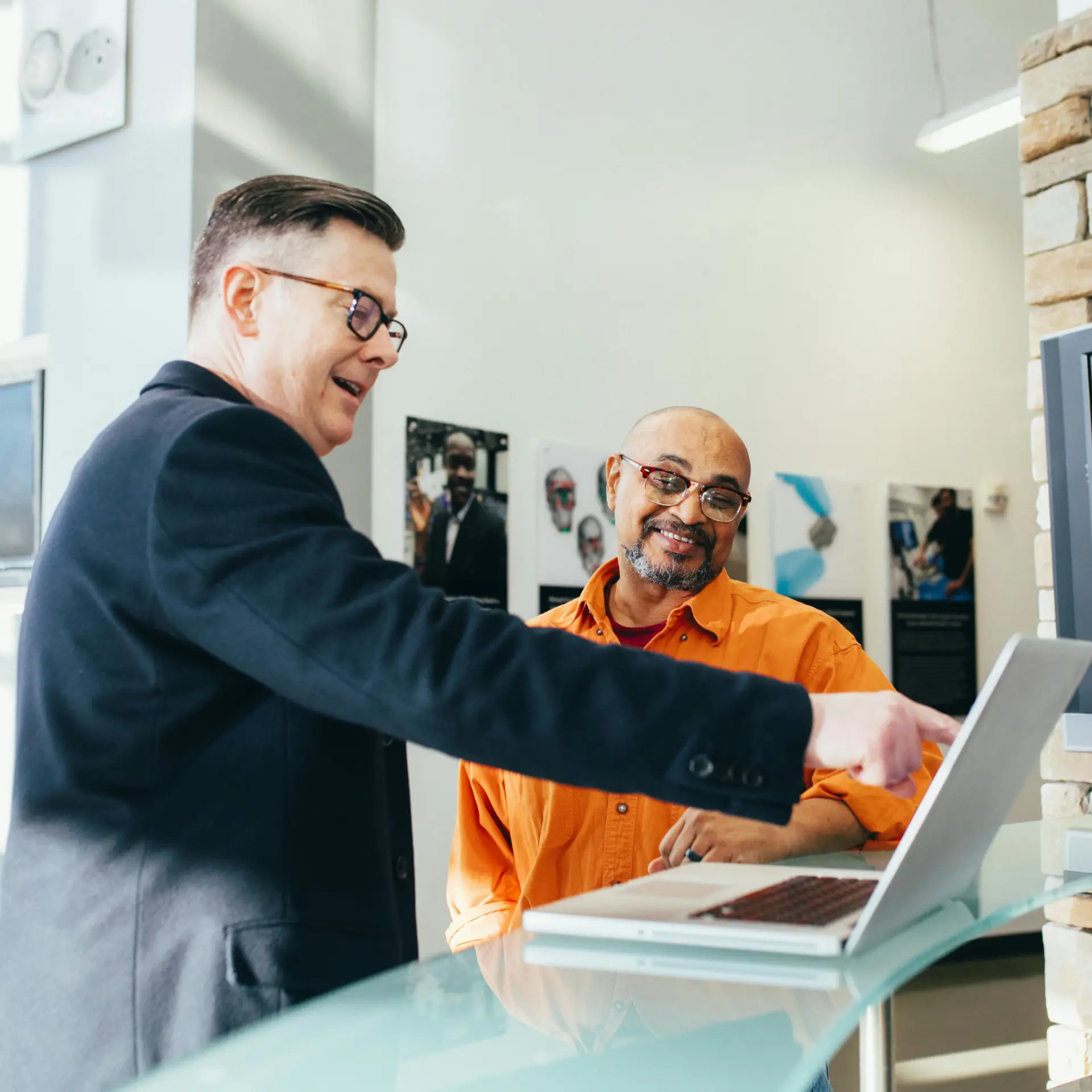 A gentleman pointing to a laptop screen to show a second gentleman something.